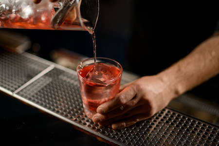 Bartender pouring a alcoholic drink from the measuring cup to the glass through the strainer filterの写真素材