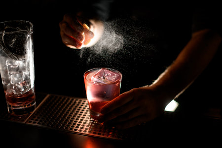 Bartender spraying on the alcoholic drink with the orange zest juice on the bar counter
