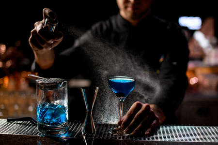 Professional bartender spraying on the blue alcoholic drink with a bitter to serve it on the bar counterの写真素材