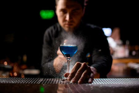 Bartender spraying on the blue alcoholic drink with a bitter to serve itの写真素材