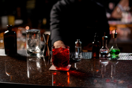 Professional male bartender serving the red alcoholic cocktail with ice cubes