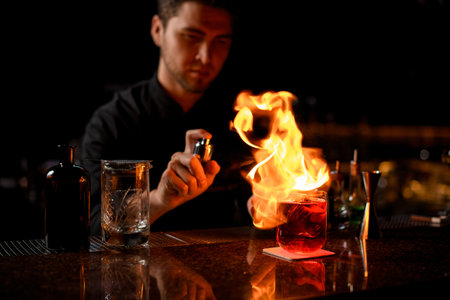 Male bartender serving the red alcoholic cocktail with ice cubes under the fire