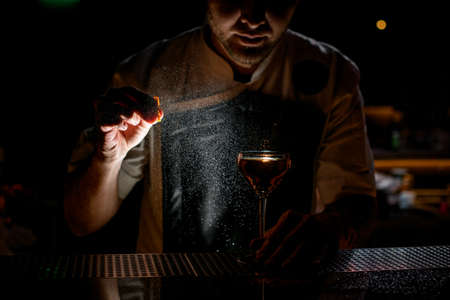 Bartender spraying on the brown alcoholic drink with a orange zest juice in the dark on the bar counterの写真素材