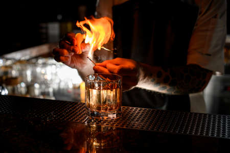 Professional male bartender serving the transparent alcoholic cocktail with ice fire sprinkling with the lemon juiceの写真素材