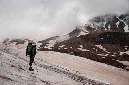 Tourist with backpack and sticks looks at mountainの写真素材