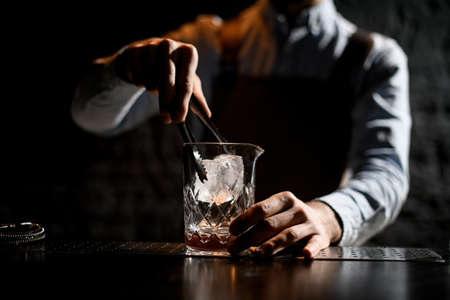 Professional bartender putting ice cube with twezzers to the glassの写真素材