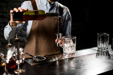 Male bartender pouring a alcoholic drink from the bottle to a steel jiggerの写真素材