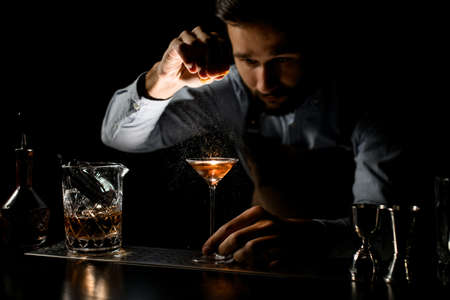Professional bartender spraying on a golden alcoholic drink in a martini glass with orage zest juiceの写真素材
