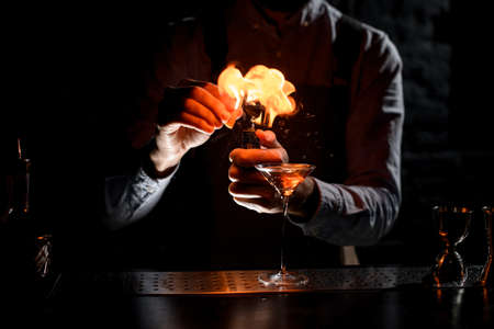 Bartender spraying on a lighter with orage zest juice to golden alcoholic drink in a martini glassの写真素材