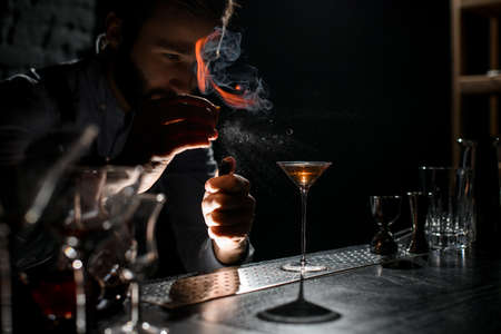 Professional male bartender spraying on a lighter with orage zest juice to the golden alcoholic drink in a martini glassの写真素材