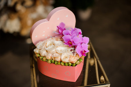 Heart shape box full of creamy color roses with the closed buds and branch of the pink orchids in the background of flower shopの写真素材