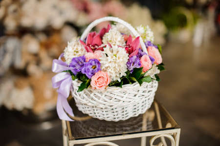 White basket with purple roses, white hyacinth and juicy pink orchids on the table in the blurred background of flower shopの写真素材