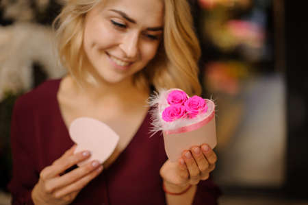 Smiling girl holding a little heart shape box full of white feathers and pink rosesの写真素材