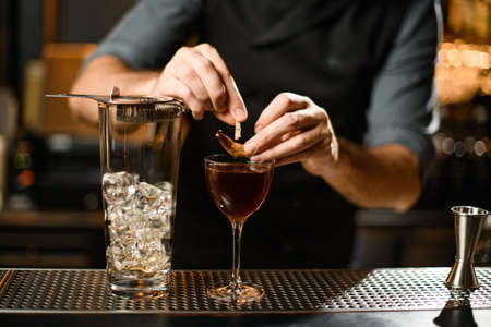 Professional bartender decorating a brown cocktail in the glass with a dried leaf by a pin on the bar counterの写真素材