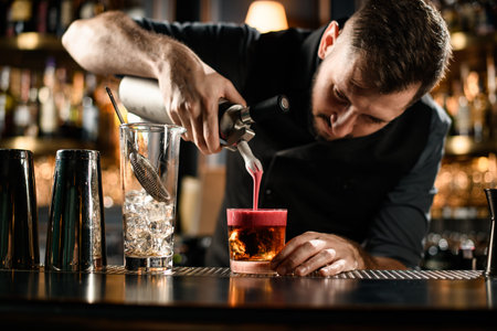 Bartender adding a smooth pink scum to the golden brown cocktail in the glass