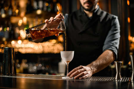 Close-up of male bartender in uniform pouring alcohol drink from stainless steel strainerの写真素材