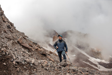 Man climbing up on the rocky mountain hill under the white fog