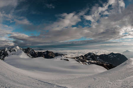 Panorama of the mountains covered by snow under the evening sky with cloudsの写真素材