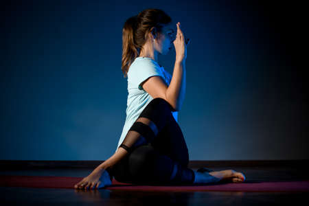Girl in sport clothes practicing yoga in a studio room in the complicated poseの写真素材