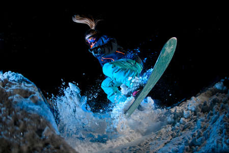 Woman snowboarder with long hair doing stunts on a snowboard on blue light backgroundの写真素材