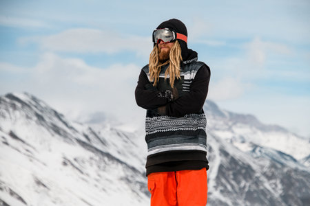 Male tourist with dreadlocks and beard in winter clothes stands in snowy mountains