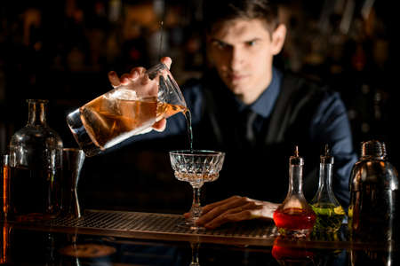 bartender gently starts pouring a cocktail into a wineglassの写真素材