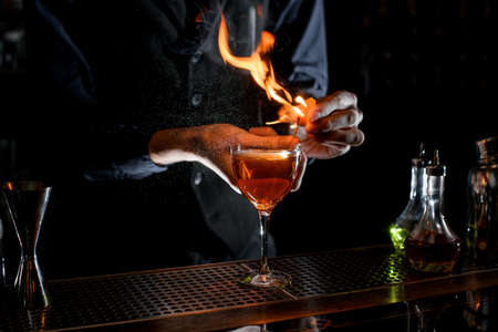 close-up of cocktail glass which bartender sprinkling by juice of citrus and sets fire.の写真素材