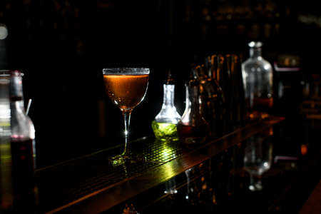 Wineglass of brown alcoholic drink stands at the bar in restaurant. Several bottles of different alcoholic drinks standing in the background.の写真素材