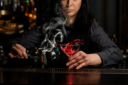 bartender girl holds smoking wand and glass with splashing drink.