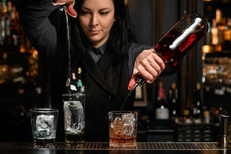 bartender girl holds bottles with drink and professional pours it into glass with ice.の写真素材