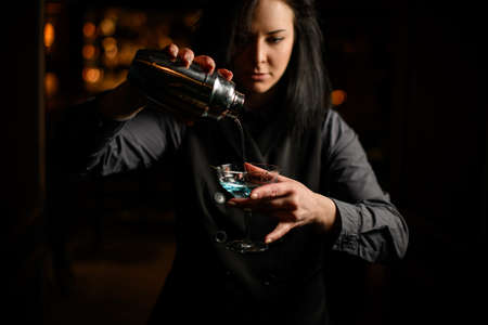 woman bartender pours blue alcoholic cocktails into wineglassの写真素材