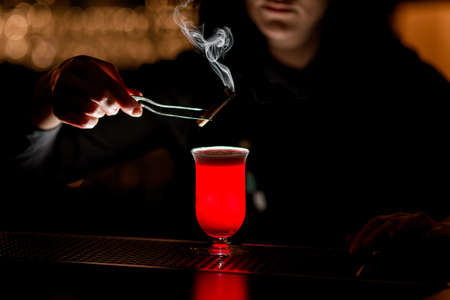 bartender hold tweezer with smoking wand over glass.の写真素材