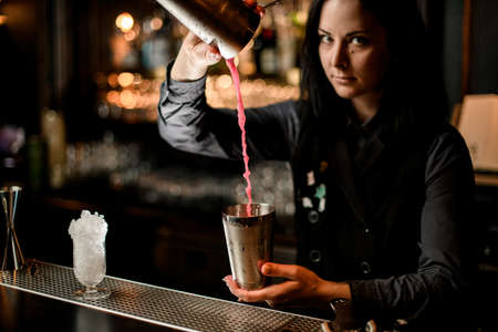young brunette woman barman pours cocktail in shakerの写真素材
