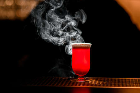 Bright red cocktail in glass stands at the bar. Smoke over glass.の写真素材
