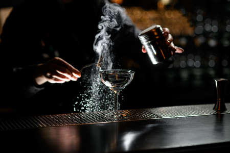 glass with clear liquid stand on bar. Bartender in background.の写真素材