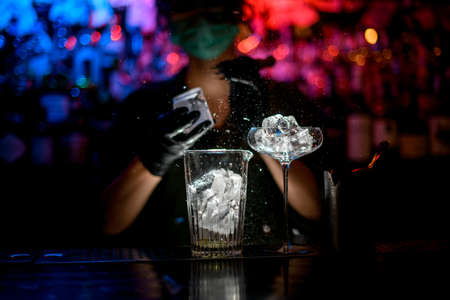 Close-up. Woman barman in medical mask and black gloves with special device accurate breaks pieces of ice.の写真素材