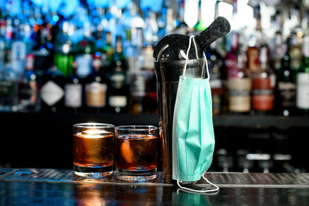 Glasses and tools for making cocktail stand on bar counter. Medical mask for prophylaxis and...