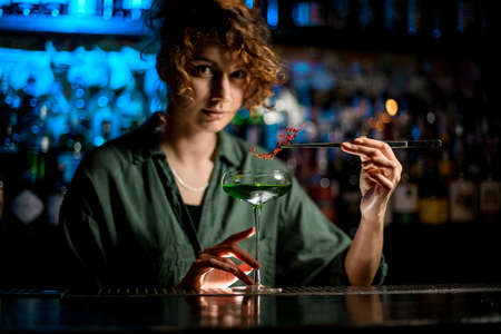 young woman at bar holds glass with cocktail and decorates itの写真素材