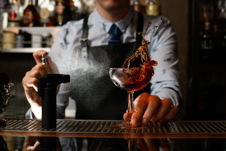 Professional bartender spray on splashing cold alcoholic drink on bar counter.