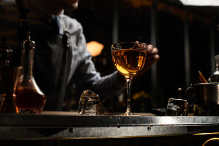 Close-up of glass with brown alcoholic drink and piece of ice on bar counter.の写真素材
