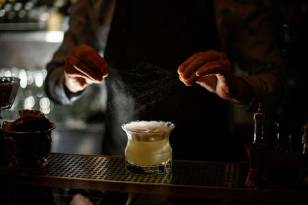 bartender sprinkles citrus juice on finished cocktail in glass.の写真素材