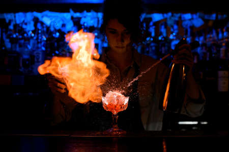 woman bartender expressive pouring cocktail from steel siphon to glass on bar counter.の写真素材