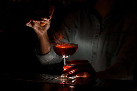 Woman barman gently sprinkles citrus juice on wineglass with cocktail at bar