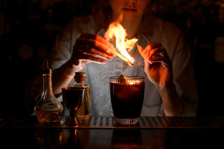 glass with red cocktail on which female bartender sprinkles by citrus and make fire over it.の写真素材