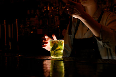 Fresh cocktail caipirinha stand on bar counter. Woman bartender behind bar holds steel madler in...