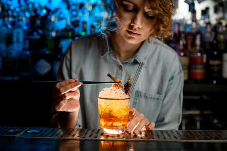 Lady bartender accurate decorates bright cocktail like negroni using tweezers.の写真素材