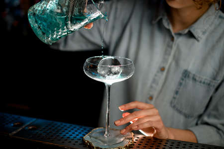 Close-up woman at bar accurate pours cocktail into glass with ice.の写真素材