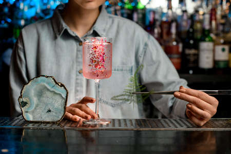 Lady barman begin to decorate glass with rose cocktail by piece of green plant.の写真素材