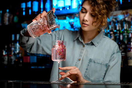 Young lady bartender pours pink cocktail into wineglassの写真素材