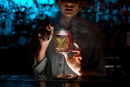 Woman bartender sprinkles on glass with fresh pink cocktail.の写真素材